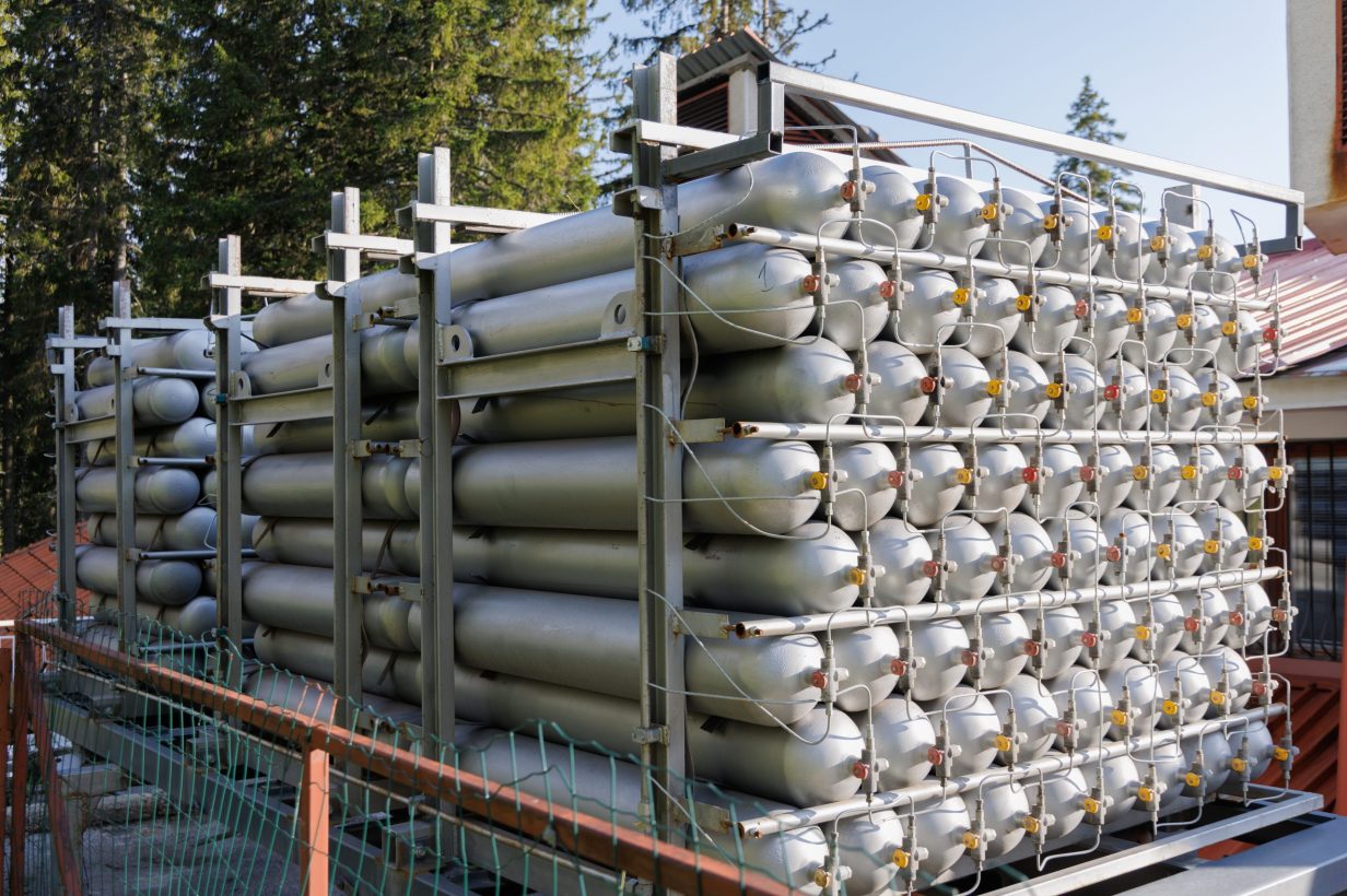 A lot of different small metal bottles filled with gas or gasoline are stacked in large piles and illuminated by the bright warm daytime sun